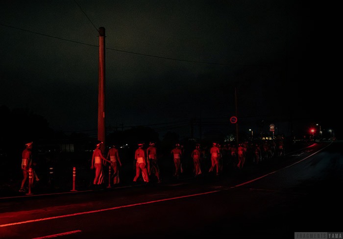 神社の外を歩いている男たちが車の赤いライトに照らされている