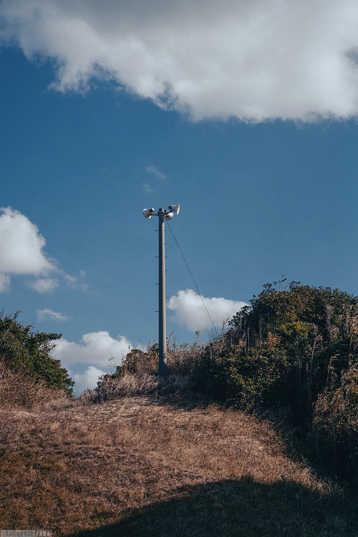 枯れ草の丘に立つスピーカー、その向こうに青空。