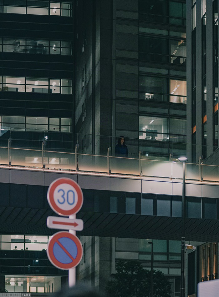 夜のビル群、歩道橋に黒い服を来た人の姿が見える